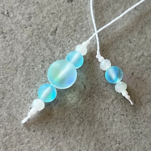 May include: A white string with iridescent blue and white beads strung on it. The beads are round and have a smooth, polished finish.