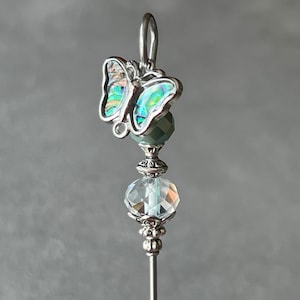 May include: A silver butterfly charm with iridescent wings and a clear crystal bead hangs from a silver pin.