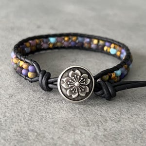 May include: A multi-colored beaded bracelet with a black leather strap and a silver flower button closure.