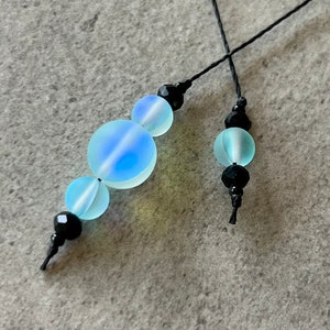 May include: A pair of beaded necklaces with iridescent blue glass beads and black beads. The necklaces are tied with black string.