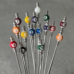 May include: A set of 14 silver cocktail picks with colorful billiard ball-shaped tops. Each ball is numbered 1 through 14.