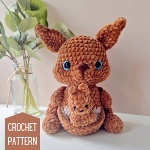 May include: Crochet pattern for a brown plush kangaroo holding a smaller brown plush joey in its pouch. The kangaroos have blue eyes and brown noses.
