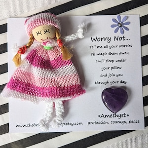 May include: A handmade worry doll with pink and white striped clothing and a purple amethyst heart. The doll is holding a flower and the text reads "Worry Not... Tell me all your worries I'll magic them away I will sleep under your pillow and join you through your day. Amethyst. protection, courage, peace"