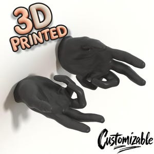 Könnte beinhalten: Zwei schwarze, 3D-gedruckte Handskulpturen, die jeweils die 'OK'-Geste bilden, auf einer weißen Oberfläche montiert. Die Worte "3D PRINTED" stehen in einer 3D-Schrift über den Händen, und "Customizable" steht in einer Schrift darunter.