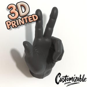 May include: A 3D-printed, matte black hand sculpture in a peace sign gesture. The words "3D PRINTED" are in 3D lettering above the hand, and the word "Customizable" is written in cursive below.