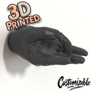 以下が含まれることがあります： わずかに曲がった指を持つ、3Dプリントされた濃い灰色の手。 「3D PRINTED」の文字が手の上の3Dスタイルのフォントで表示されています。 手の下には、「Customizable」の文字が筆記体フォントで書かれています。