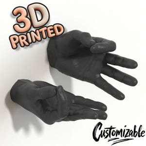 Könnte beinhalten: Zwei 3D-gedruckte schwarze Handskulpturen, eine mit gespreizten Fingern und die andere in entspannter Pose. Die Worte "3D PRINTED" sind in 3D-Schrift, und "Customizable" ist in einer Schreibschrift geschrieben.