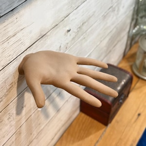 May include: A light brown plaster hand sculpture with five fingers outstretched, mounted on a white wood wall.