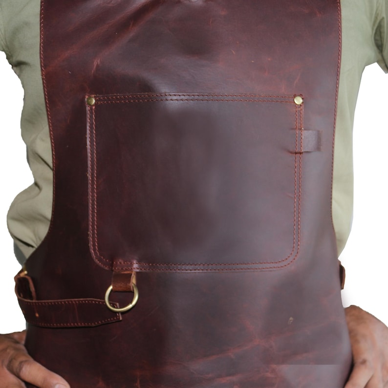May include: A brown leather apron with a large pocket and a brass D-ring on the side.