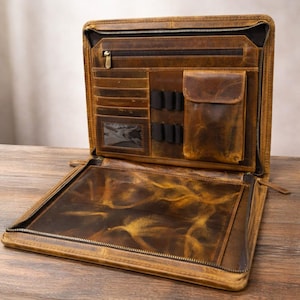 May include: Open brown leather portfolio with multiple compartments, including card slots, pen holders, and a zipped pocket. The portfolio has a distressed finish and a zip closure. The interior features a clear pocket and a large open area.