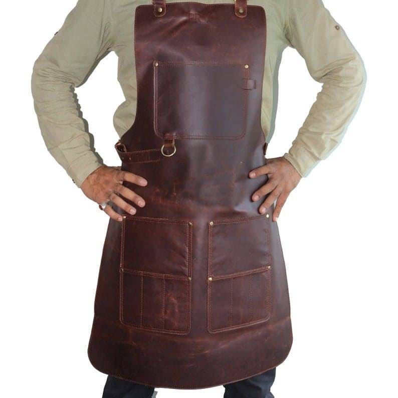 May include: A brown leather apron with multiple pockets and a brass buckle. The apron has a distressed look and is made of thick, durable leather.