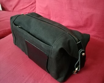 Op de afbeelding: Een zwarte toilettas van canvas en leer met een ritssluiting en een klein leren patch aan de voorkant.