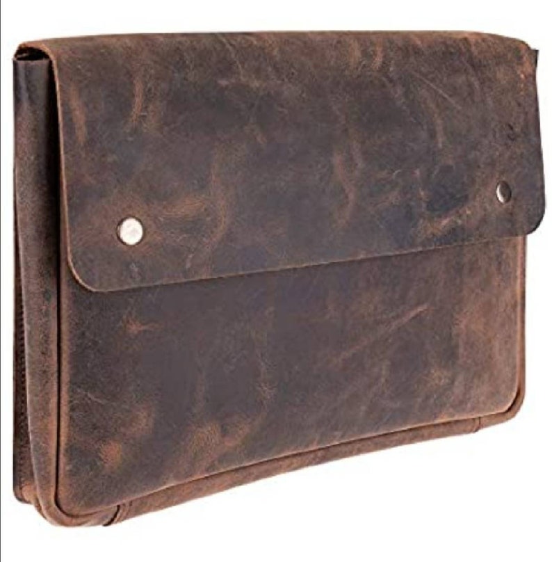 May include: A brown leather laptop sleeve with a flap closure and two silver snaps. The sleeve has a distressed look and is made of a durable material.