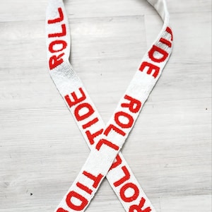 May include: White beaded bag strap with red "Roll Tide" lettering. The strap has gold clasps on each end.