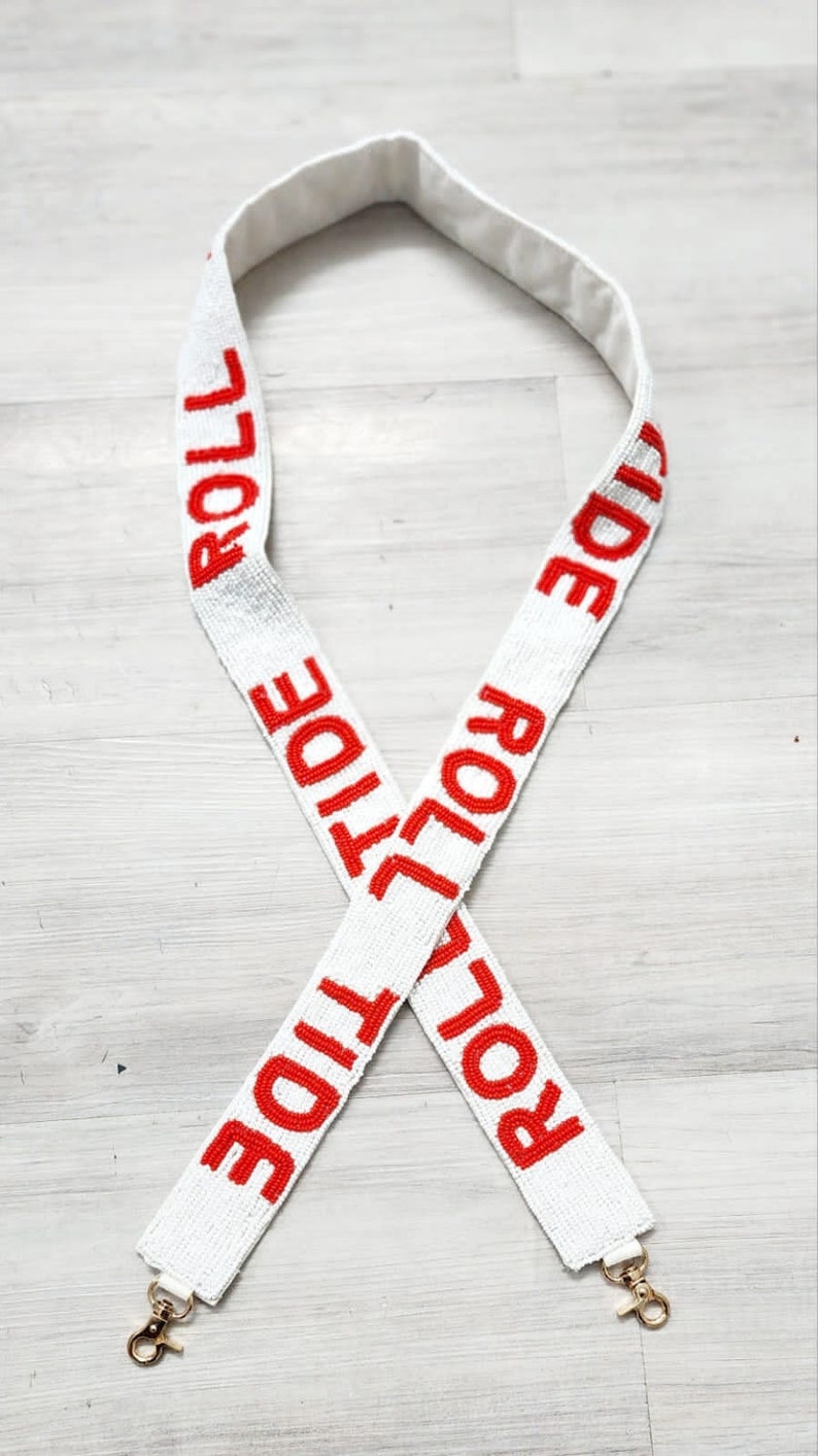 May include: White beaded bag strap with red "Roll Tide" lettering. The strap has gold clasps on each end.