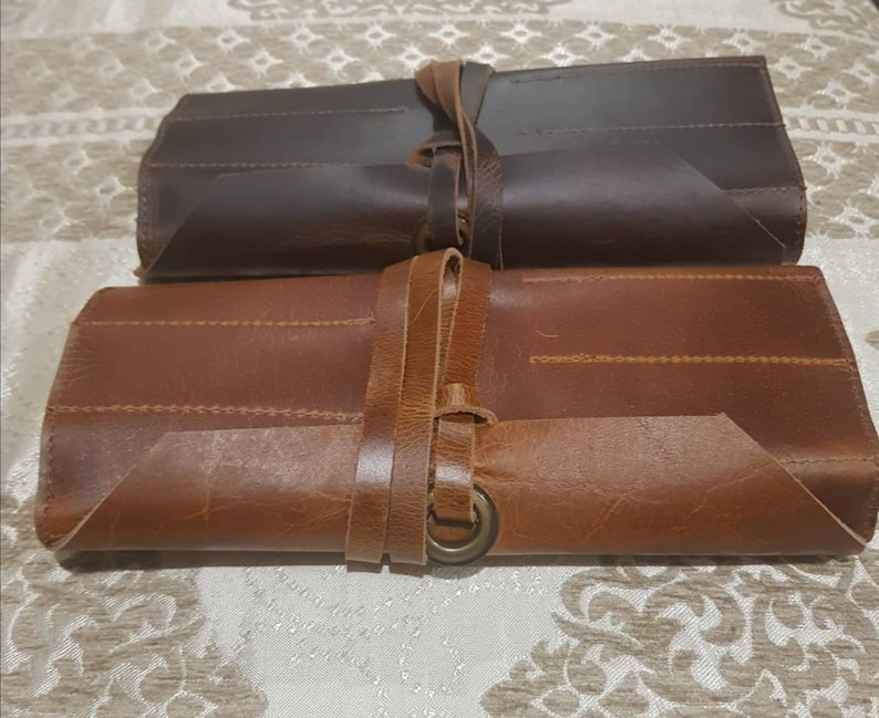 May include: Two leather tool rolls, one brown and one dark brown, with a strap and buckle closure. The rolls are rolled up and tied with a leather strap.