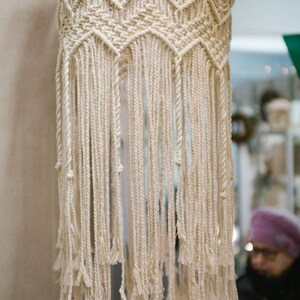 May include: A white macrame hanging lampshade with a geometric pattern and long fringe.