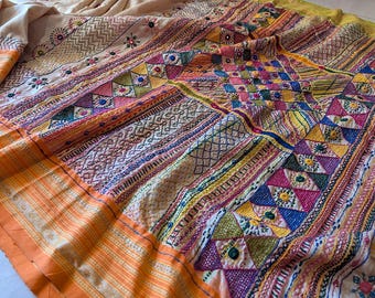 May include: A colorful textile with intricate embroidery. The design features geometric patterns, floral motifs, and various stitching techniques in shades of orange, yellow, pink, blue, and green. The fabric has an orange border.