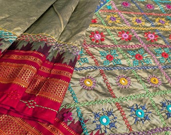 May include: Olive green fabric with intricate embroidery in a geometric pattern. The design incorporates colorful floral and mirror accents. A red border with gold detailing adds a striking contrast to the main fabric.