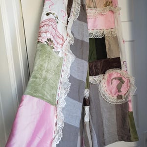 May include: A patchwork skirt with a variety of fabrics and colours. The skirt features squares of pink, green, brown, and grey fabrics, some with floral and palm tree patterns. White lace trim edges the skirt.