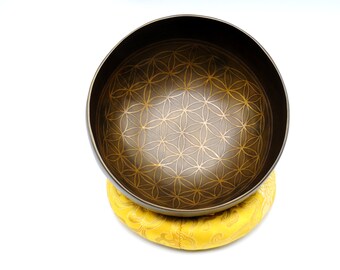 Può includere: Una ciotola cantate marrone scuro con un disegno dorato del fiore della vita all'interno. La ciotola è appoggiata su un cuscino giallo.