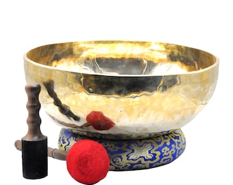 May include: A large, golden singing bowl with a wooden mallet and a red felt striker. The bowl is resting on a blue and gold patterned cushion.