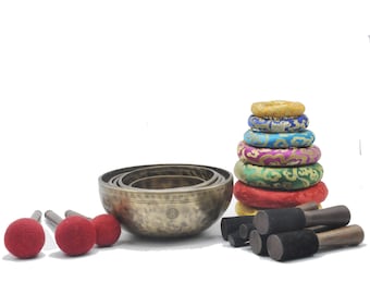 May include: A set of seven singing bowls with a variety of colorful cushions, and three wooden mallets with red felt heads. The bowls are stacked in a pyramid shape, with the largest bowl at the bottom.