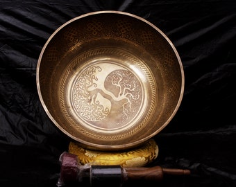 May include: A large, golden singing bowl with a tree of life design. The bowl is resting on a cushion with a matching design. A wooden striker is included.