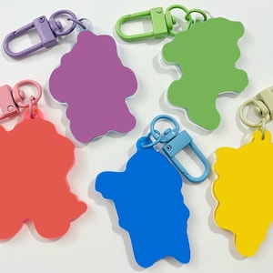 May include: Five colorful keychains with different shaped charms. The charms are pink, purple, green, blue, and yellow. Each keychain has a metal clasp.