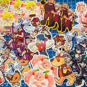 May include: A collection of colorful stickers featuring various characters and designs. The stickers are on a blue background and include characters with wings, a rainbow, a dog, and a character with a bandage. The stickers are perfect for decorating laptops, water bottles, and other items.
