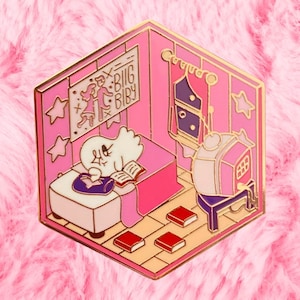 Puede incluir: Un pin de esmalte rosa y dorado en forma hexagonal. El pin representa una habitación de dibujos animados con una figura fantasmal leyendo en la cama. La habitación tiene un televisor, libros y un letrero que dice "BIG BABY".