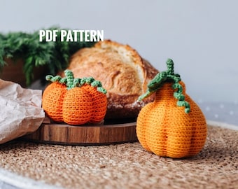 May include: Two crocheted orange pumpkins with green stems and leaves on a wooden tray. The pumpkins are sitting on a woven brown mat. The text "PDF PATTERN" is visible in the top left corner of the image.