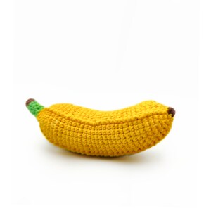 May include: A crocheted banana toy made of yellow, green, and brown yarn. The banana is a soft, plush toy that is perfect for babies and toddlers.