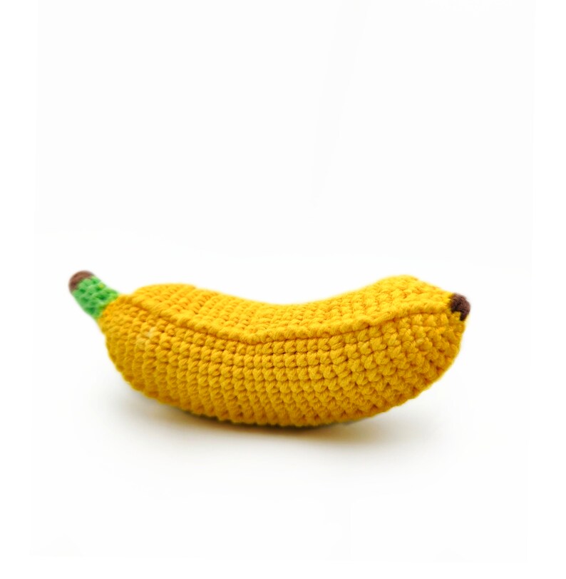 May include: A crocheted banana toy made of yellow, green, and brown yarn. The banana is a soft, plush toy that is perfect for babies and toddlers.