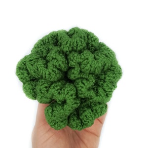 May include: A green crocheted hair scrunchie in the shape of a flower. The scrunchie is made of soft yarn and has a textured surface.