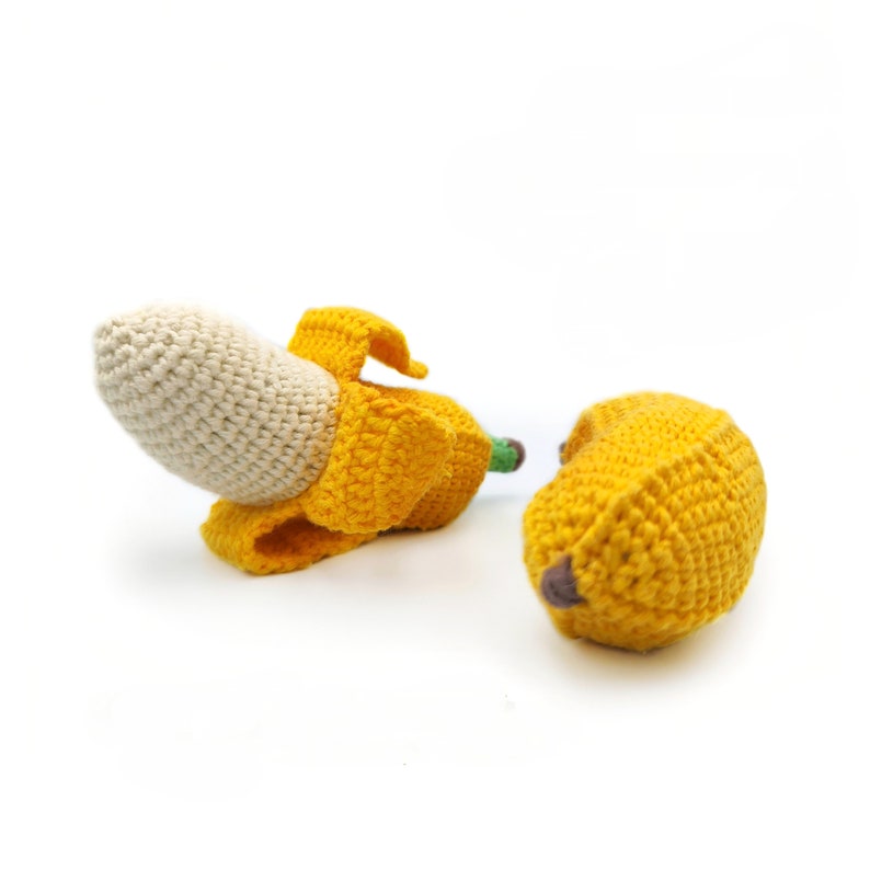 May include: Two crocheted banana toys. One banana is yellow and has a brown stem. The other banana is partially peeled and has a white inside and a yellow peel.