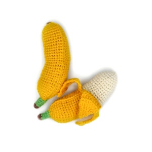 May include: Two crocheted bananas, one yellow and one with a white tip, are arranged on a white background. The bananas are made with a textured yarn and have a realistic appearance.