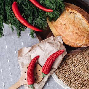 Puede incluir: Dos chiles rojos de ganchillo en una cuchara de madera y papel marr&oacute;n, junto a una hogaza de pan y un manojo de eneldo fresco.