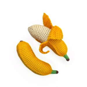 May include: Two crocheted banana toys. One banana is whole and yellow, the other is peeled and has a white crocheted inside.