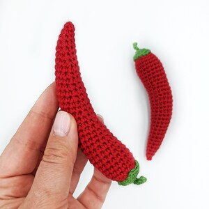Puede incluir: Dos chiles rojos de ganchillo con tapas verdes. Los chiles est&aacute;n hechos a mano y tienen una superficie texturizada.