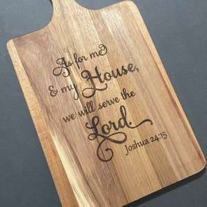 May include: A wooden cutting board with a handle, engraved with the text "As for me and my house, we will serve the Lord. Joshua 24:15".
