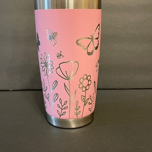 May include: A pink stainless steel tumbler with a floral design featuring butterflies, bees, and flowers. The tumbler has a silver lid.