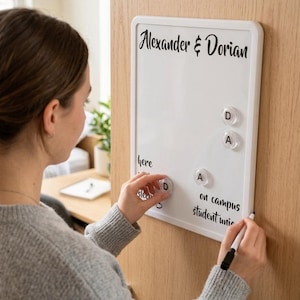 May include: A rectangular white magnetic dry erase board with a white frame. The board features the printed text Alexander & Dorian at the top, with the words here, sleep, on campus, and student union below. Four clear circular magnets with letters are attached.