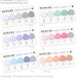 Puede incluir: Cinco paquetes de blocs de notas con notas adhesivas de diferentes colores. Cada paquete contiene cinco colores diferentes de notas adhesivas en forma de semicírculos. Los colores son gris, verde, morado, rosa, azul y naranja. El texto en los paquetes dice "Memo Me, The colour of life" y "Sticky Memos, 色彩研究所". El texto en la parte inferior de la imagen dice "Cantidad: 30 hojas de pegatinas x 5 colores por bloc, Medida del bloc: 140 mm x 67 mm".