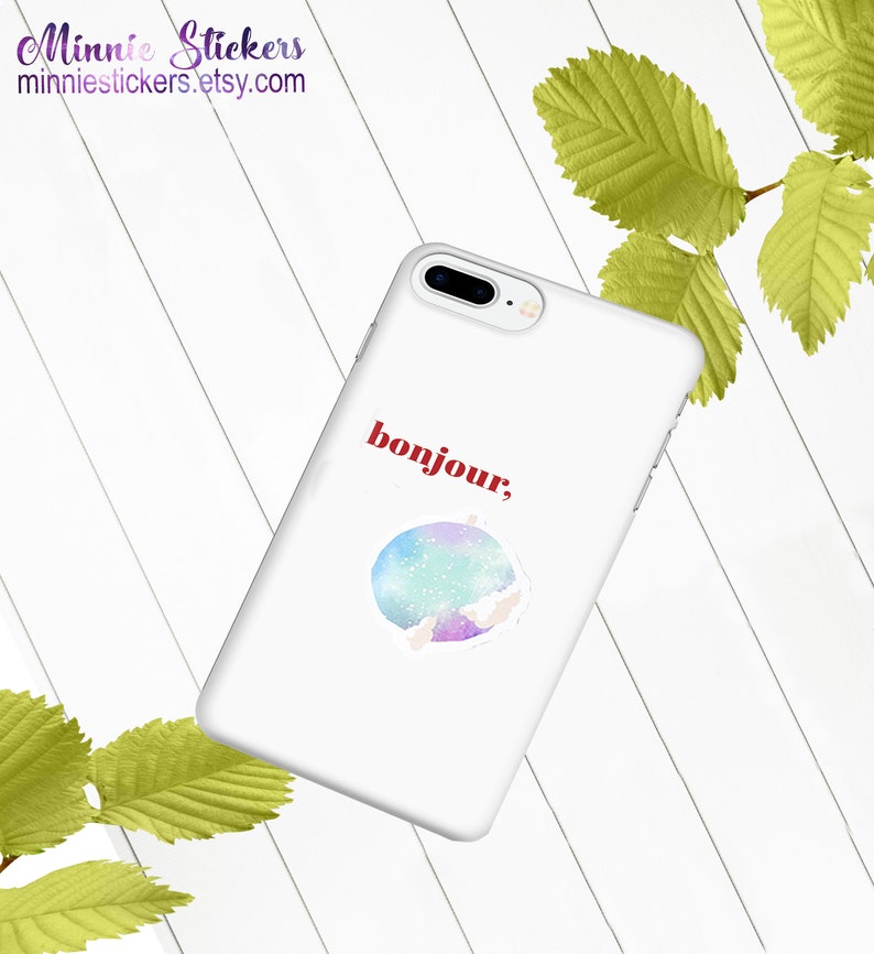 May include: White phone case with a watercolour-style sticker of a galaxy with the word "bonjour" in red text.