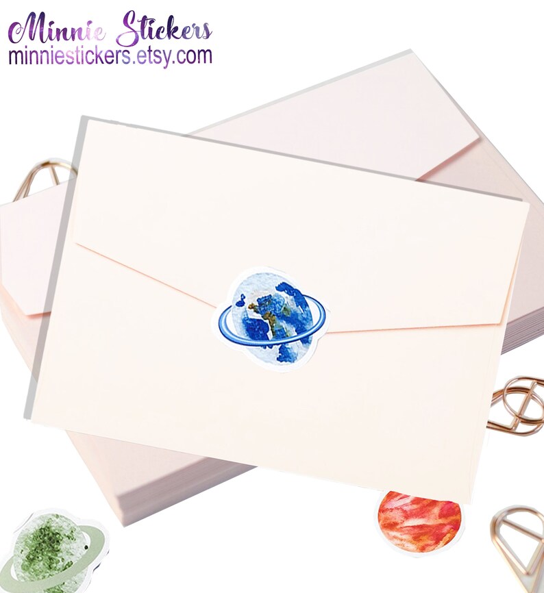 May include: A stack of pink envelopes with a blue and white watercolour sticker of the Earth with a ring around it. The sticker is on the top envelope. There are two other stickers, one green and one red, visible in the image.