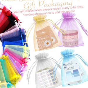 May include: An assortment of colourful organza bags filled with various items, including stickers, washi tape, and index cards. The bags are ready to be used for gift packaging.