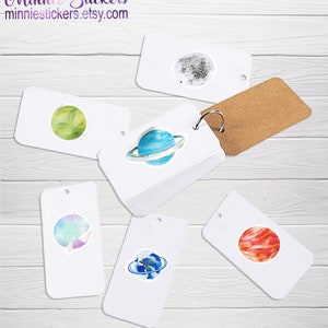 May include: A set of six white cardstock stickers featuring watercolour illustrations of planets and moons. The stickers are arranged on a light wood background. The stickers are perfect for adding a touch of whimsy to your planner, journal, or laptop.