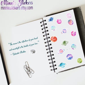 May include: A notebook with a quote about the moon and moonlight. The notebook has a spiral binding and is decorated with colourful watercolour planet stickers.