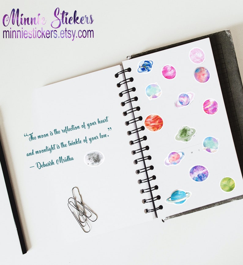 May include: A notebook with a quote about the moon and moonlight. The notebook has a spiral binding and is decorated with colourful watercolour planet stickers.